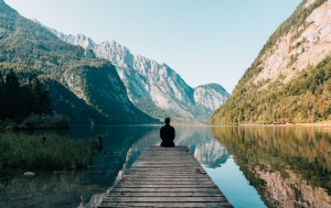 Photo of Person sitting on a dock looking out onto a lake and mountains by Simon Migaj on Unsplash