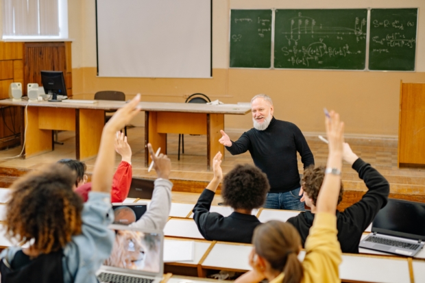 Professor teaching students with hands raised in lecture hall