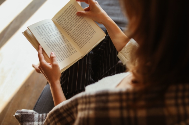 person reading book sitting on couch